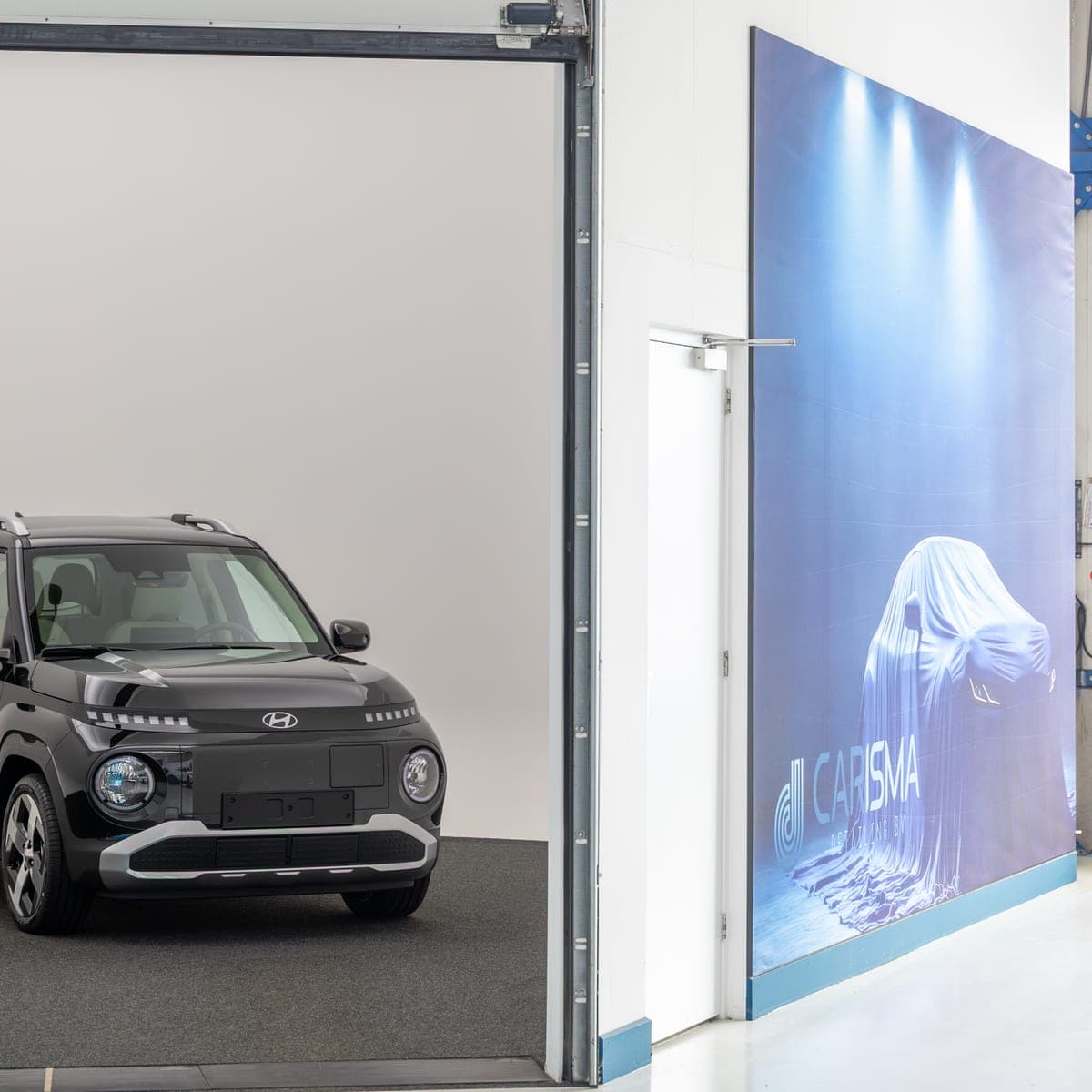 Een auto in de witte fotostudio naast een wand met het Carisma-logo