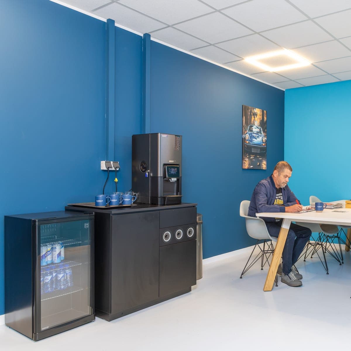 Iemand zit aan tafel in de blauwe wachtruimte met koffiehoek