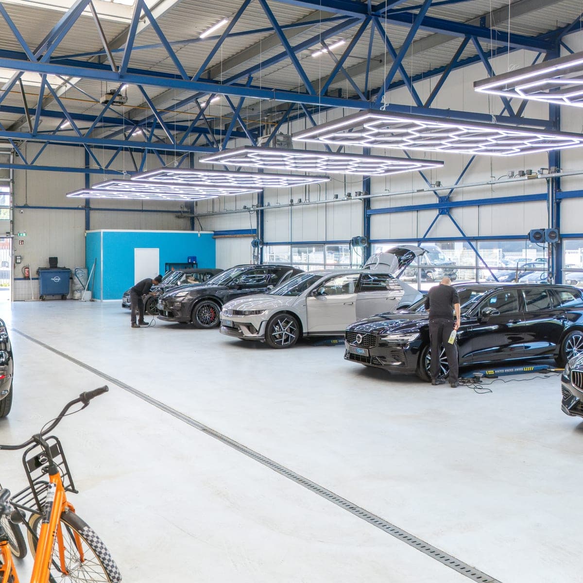 De werkplaatshal met meerdere auto’s onder de LED-verlichting en een medewerker die een auto behandelt