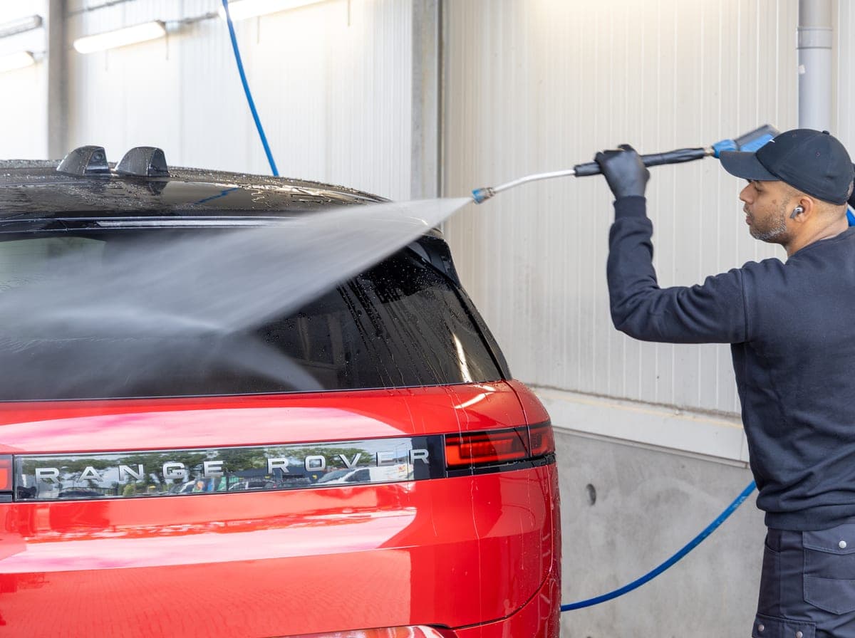 Een medewerker spoelt een rode Range Rover af met een hogedrukspuit