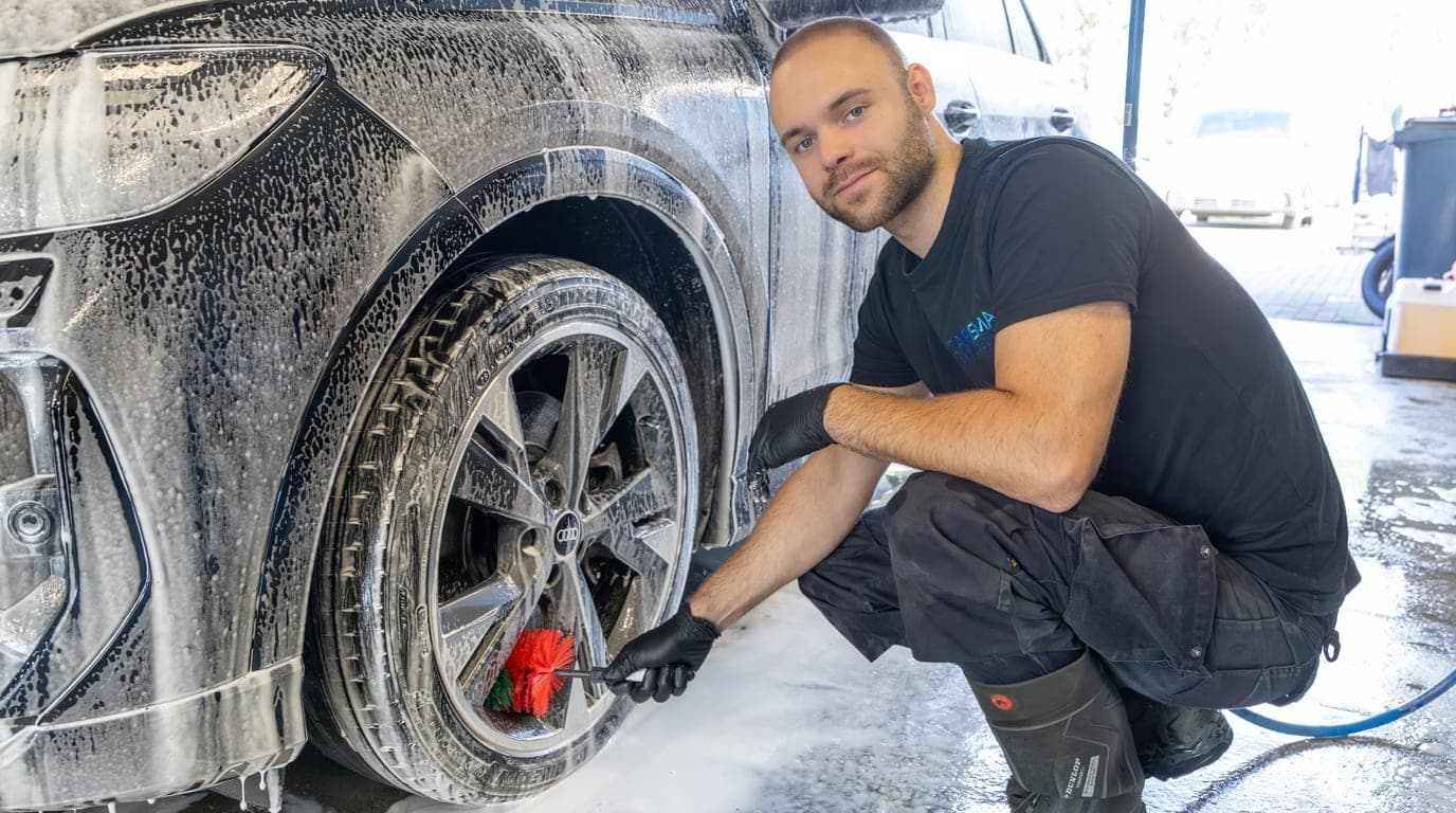 Een medewerker wast met een borstel het met schuim bedekte wiel en de wielkast van een auto
