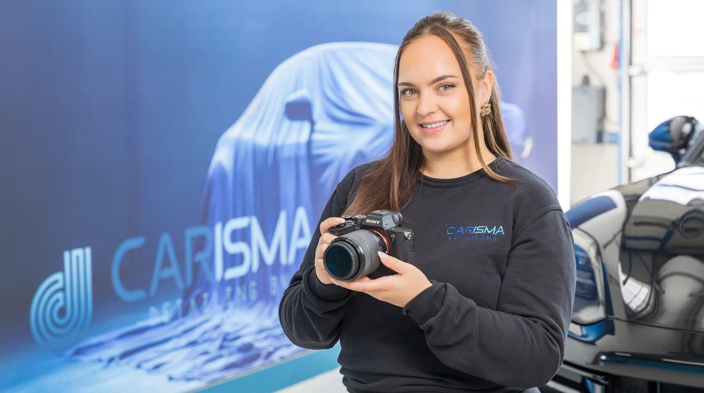Een medewerker houdt een camera vast voor een wand met het Carisma-logo