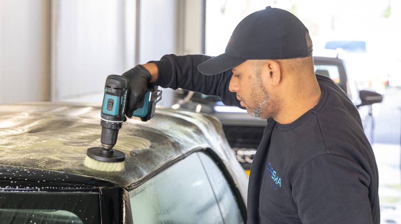 Een medewerker behandelt met een machine het natte dak van een cabriolet