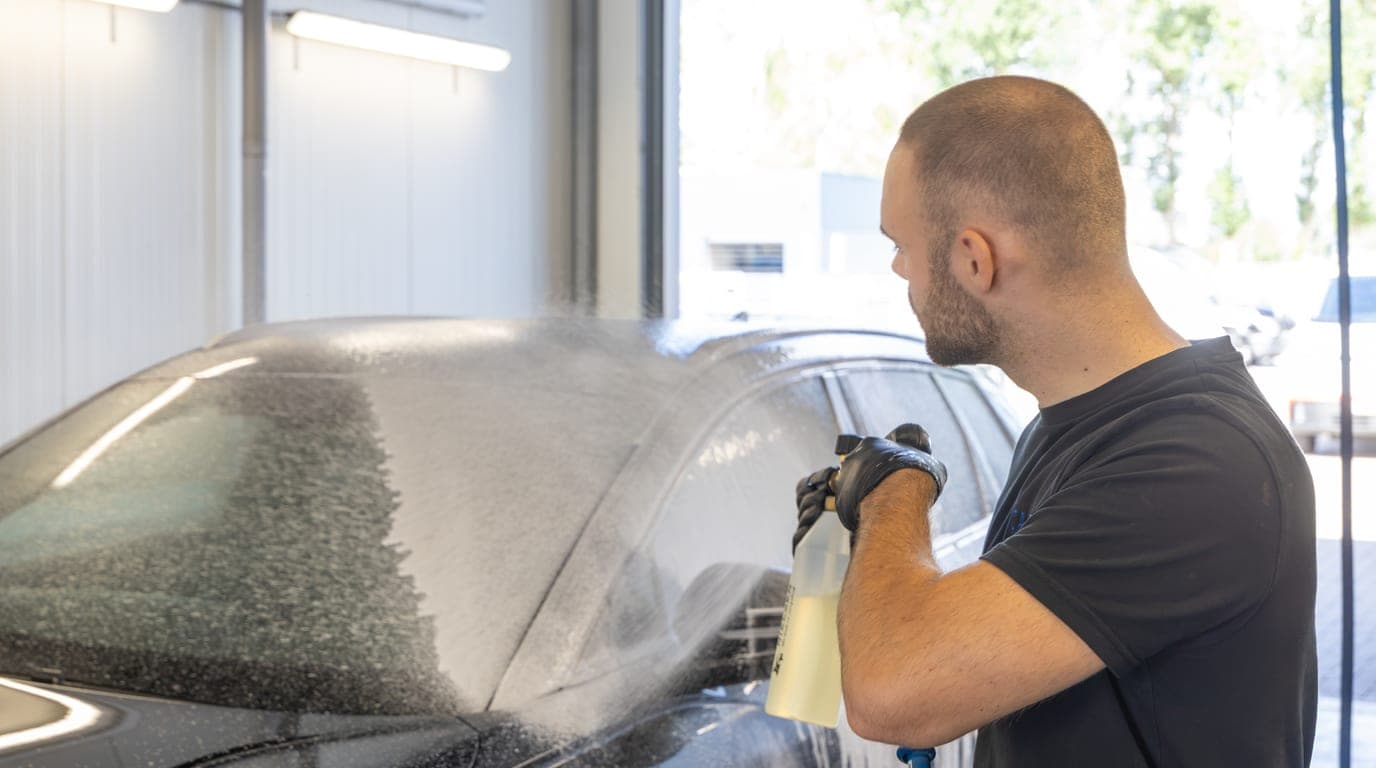 Een medewerker besproeit de motorkap van een auto met schuim