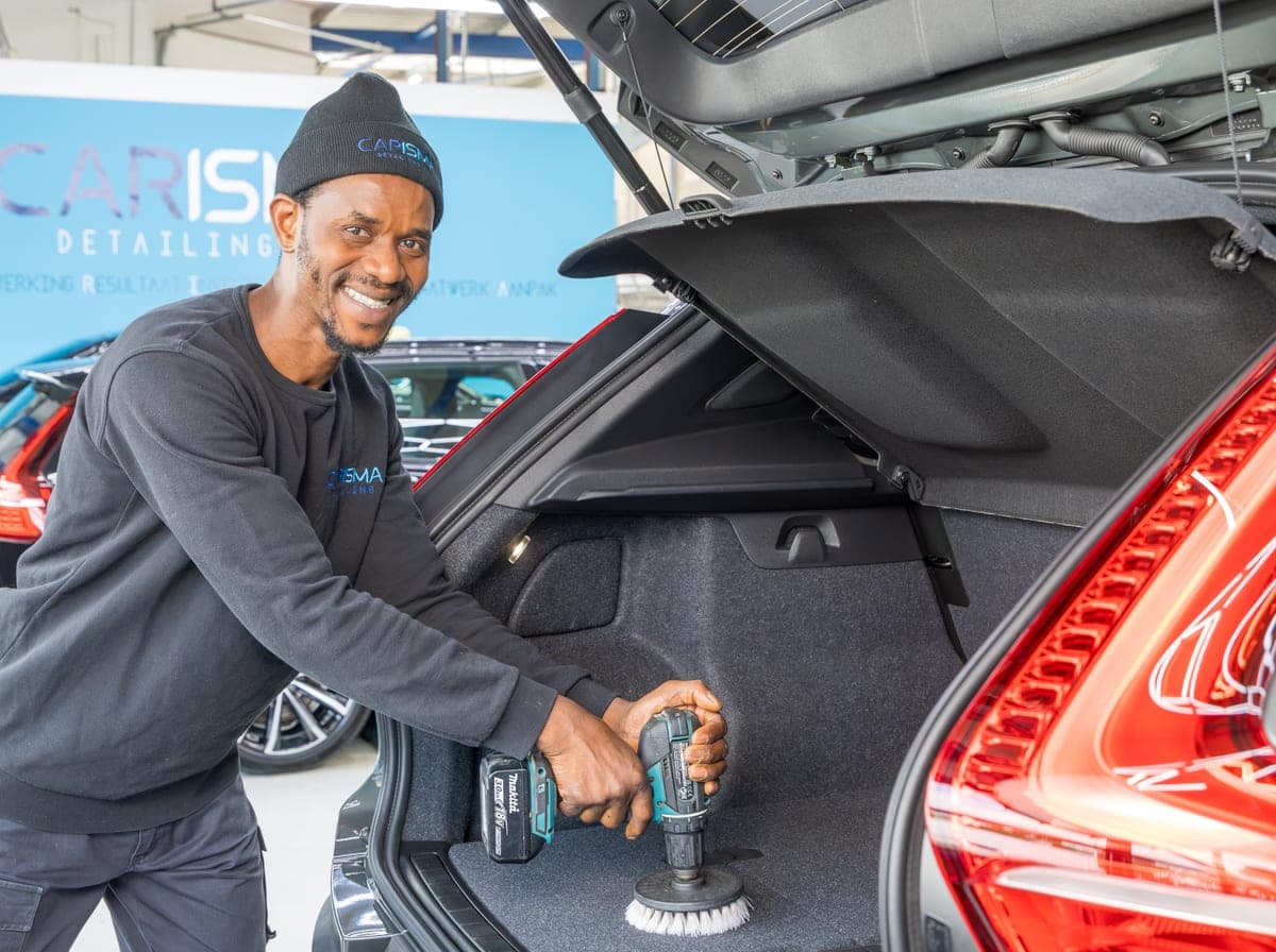Een medewerker reinigt de kofferbak van een auto met een borstel op een accuboormachine