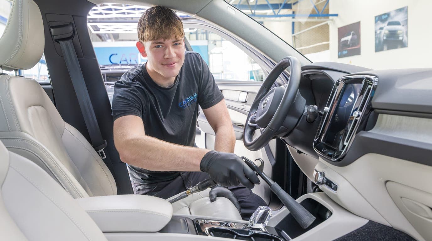 Een medewerker reinigt het interieur van een auto met witte lederen stoelen
