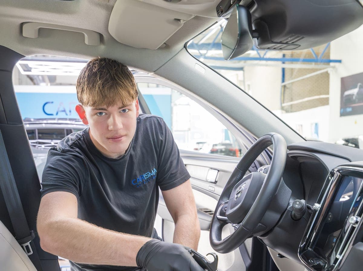 Een medewerker reinigt de middenconsole van een auto-interieur