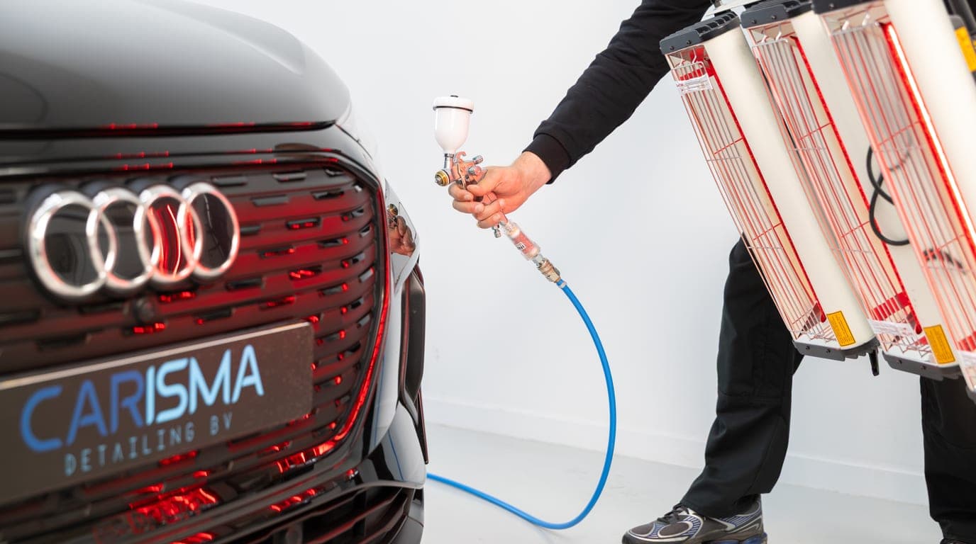 Een medewerker houdt een spuitpistool bij de voorkant van een zwarte auto