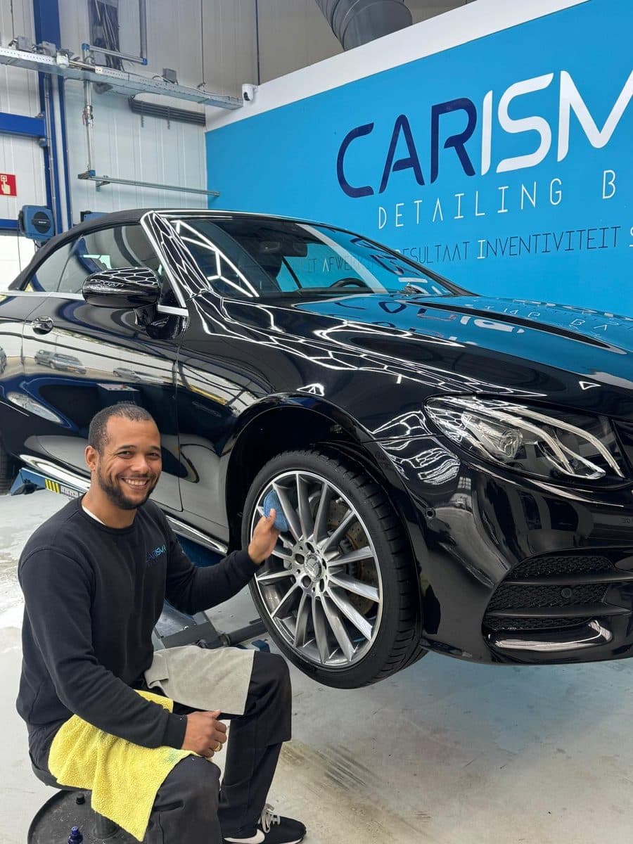 Een lachende medewerker van Carisma coat met een applicatorblokje de velg van een zwarte Mercedes in de werkplaats