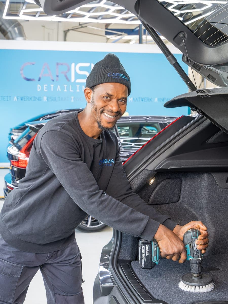 Sidi reinigt de kofferbak van een auto met een borstel op een accuboormachine
