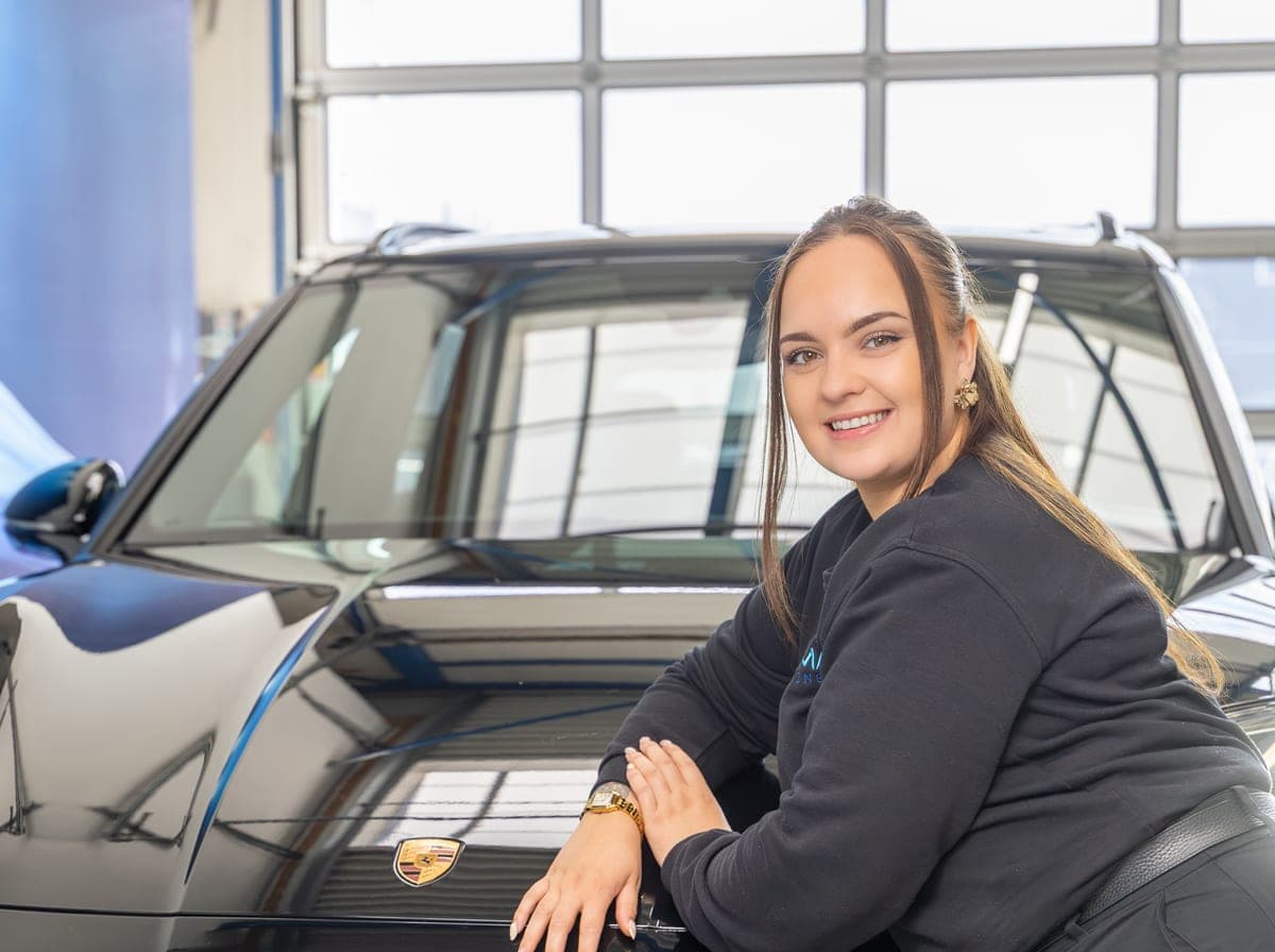 Een medewerker leunt glimlachend tegen een zwarte auto