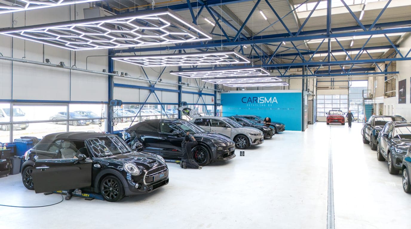 Werkplaatshal met meerdere auto’s en Carisma-wand op de achtergrond