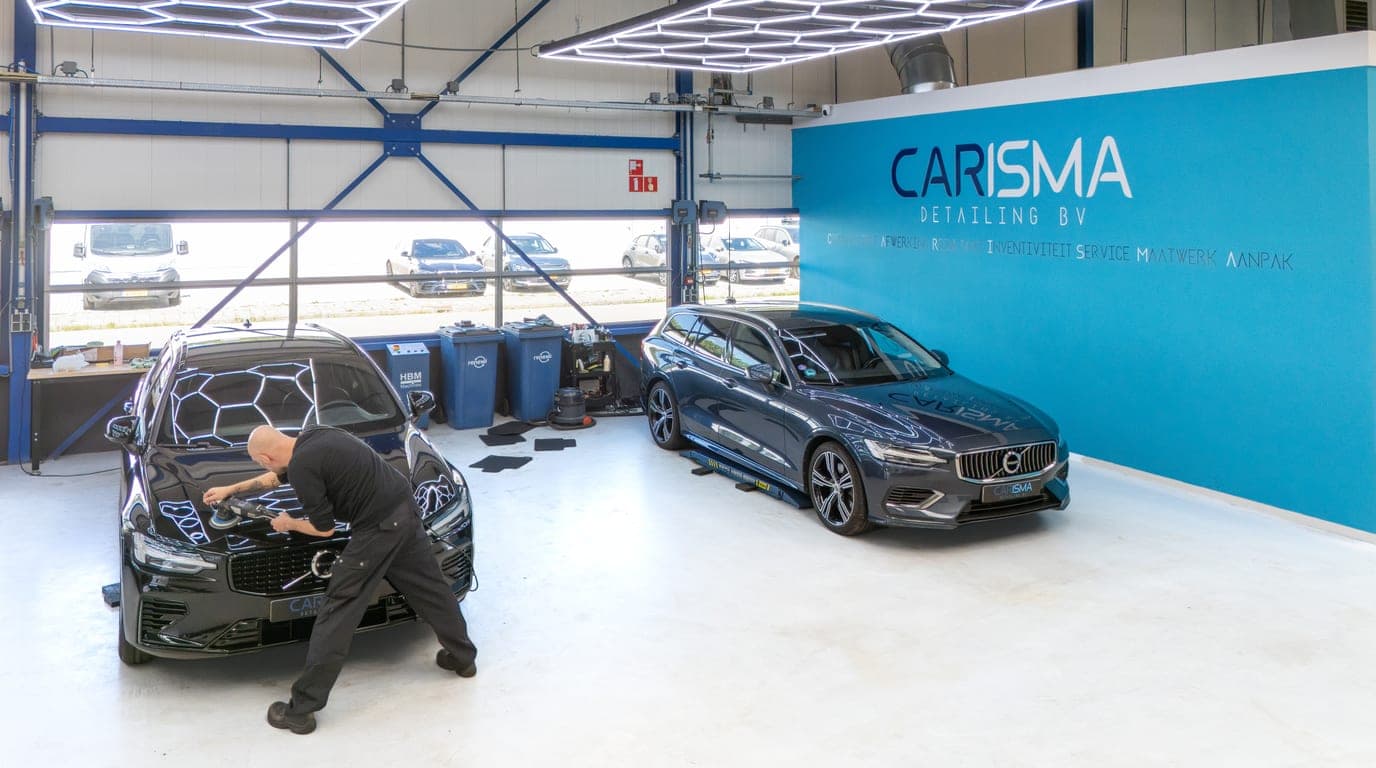 Een medewerker polijst een zwarte auto in de werkplaats