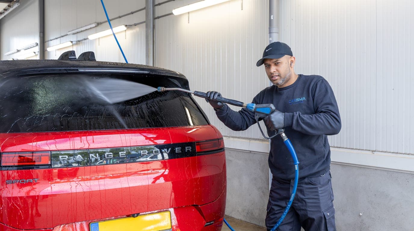 Een medewerker spoelt de achterkant van een rode Range Rover af