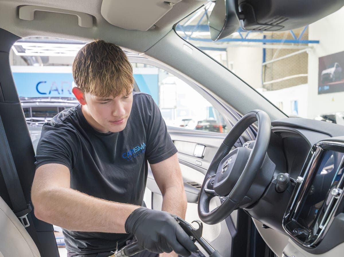 Een medewerker stofzuigt het interieur van een auto aan de bestuurderskant
