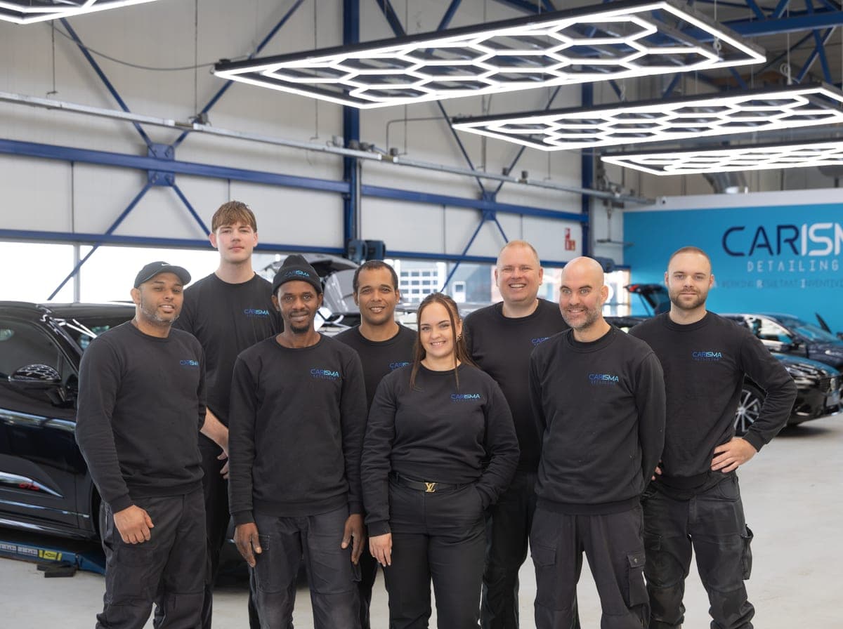 Het team poseert samen in de werkplaats onder de LED-verlichting