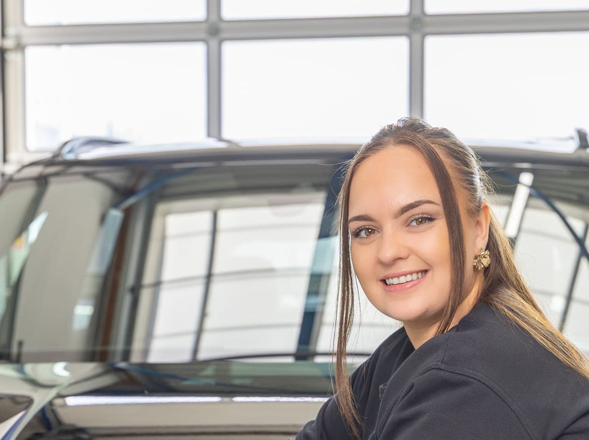 Een medewerker glimlacht naast een auto in de werkplaats