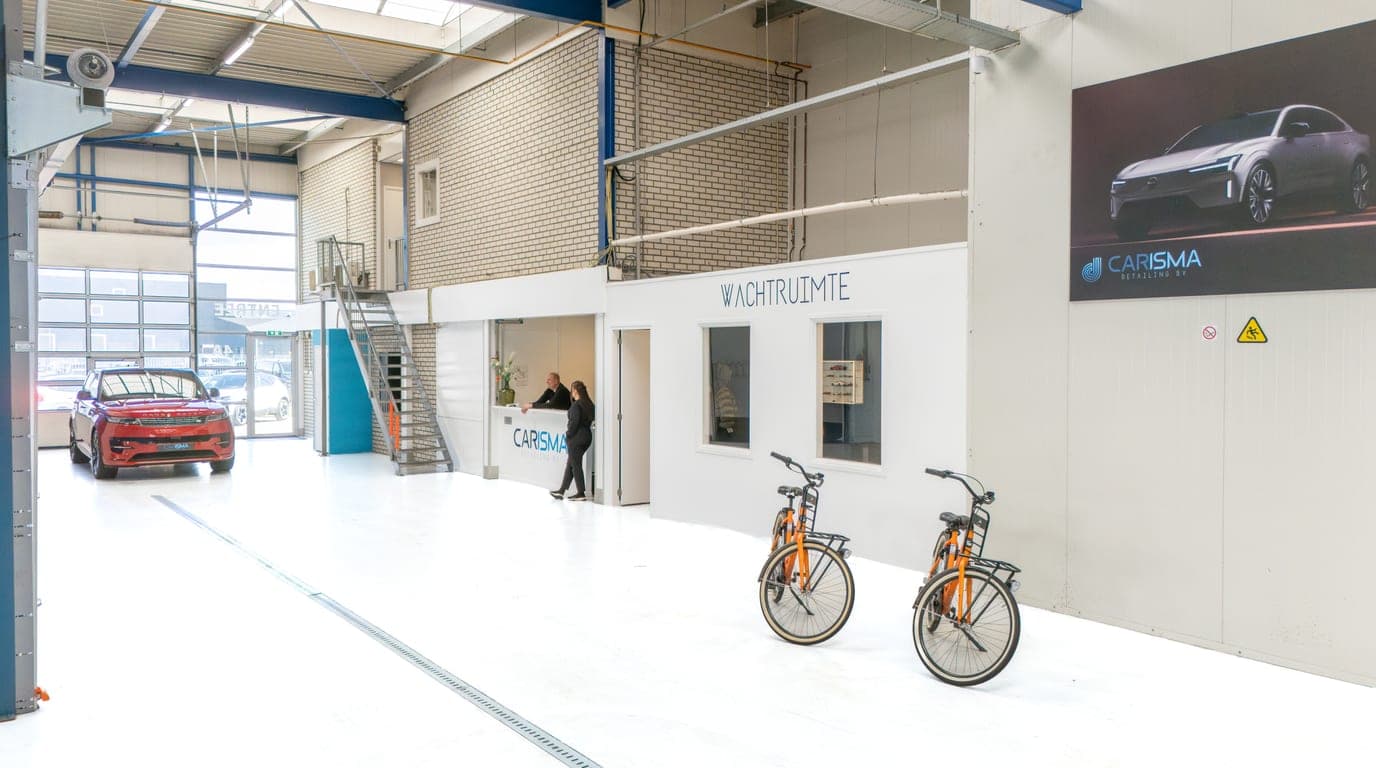 Overzicht van de werkplaats met een auto op de achtergrond en de glazen wachtruimte met twee leenfietsen ervoor
