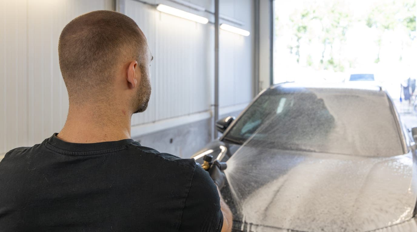 Een medewerker besproeit een auto met schuim, gezien van achteren